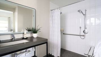 Un baño moderno con lavamanos de encimera negro, un espejo, una ducha con cabezal de ducha de mano y cortina de ducha blanca.
