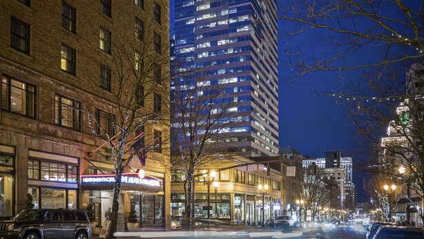 A nighttime city street with tall buildings, a tree with lights, and a car. - Heathman Hotel (Portland)