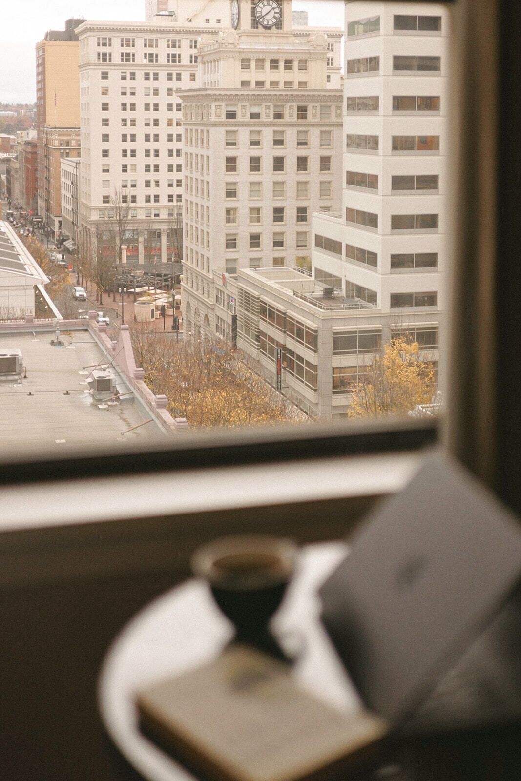 A view from a window overlooking a city street with tall buildings, a clock tower, and a bridge.