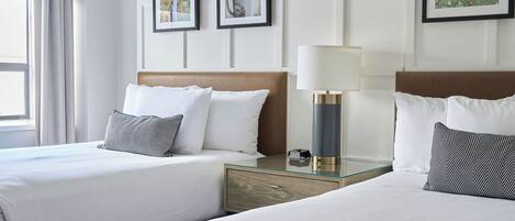 A hotel room with two beds, a nightstand with a lamp, and framed artwork on the walls.