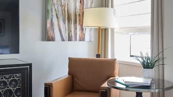 Una sala moderna con un sillón de cuero, una mesa redonda de vidrio con una lámpara, un cuadro abstracto enmarco y un televisor sobre un mueble.
