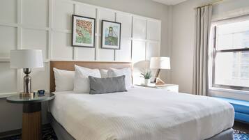 Una habitación de hotel con una cama grande, dos cuadros en la pared, una ventana con cortinas y una mesita de noche con lámpara.