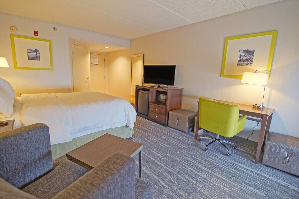 A hotel room with a bed, a desk, a chair, a television, and a small table.