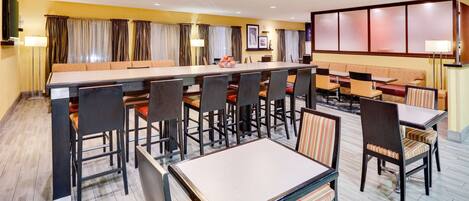 A hotel dining area with a long communal table, multiple booths, and individual tables.