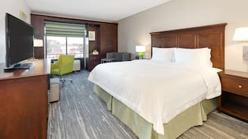 A hotel room with a large bed, a desk with a TV, a chair, and a window with blinds.