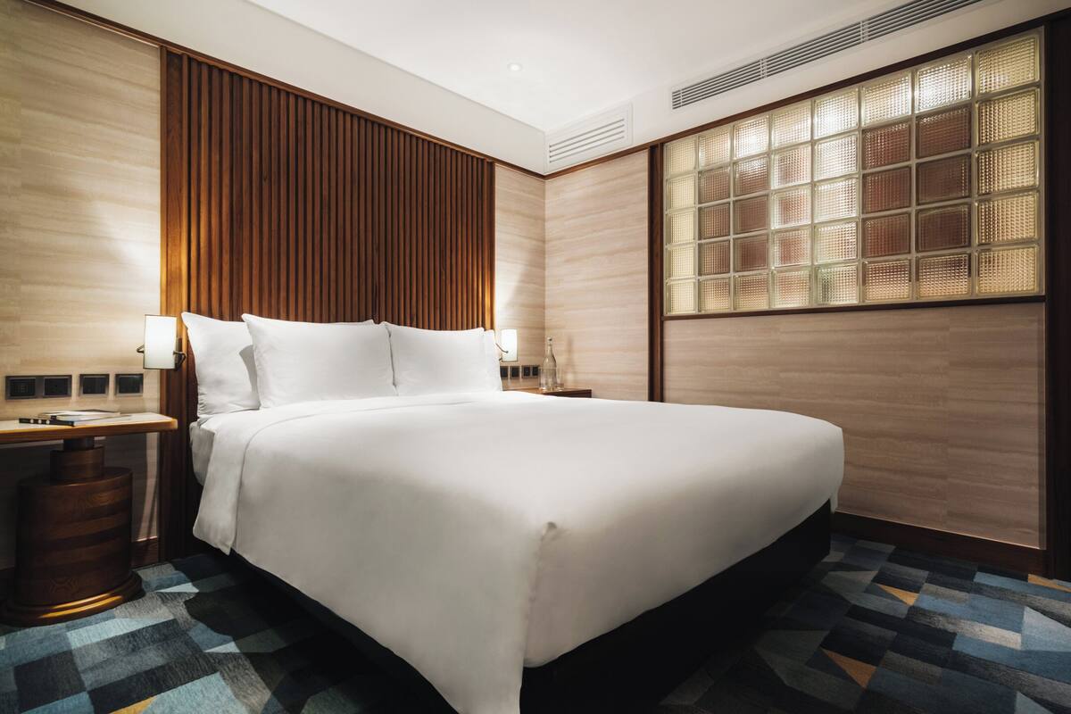 A hotel room with a large bed, wooden panel wall, and a window with a grid pattern.