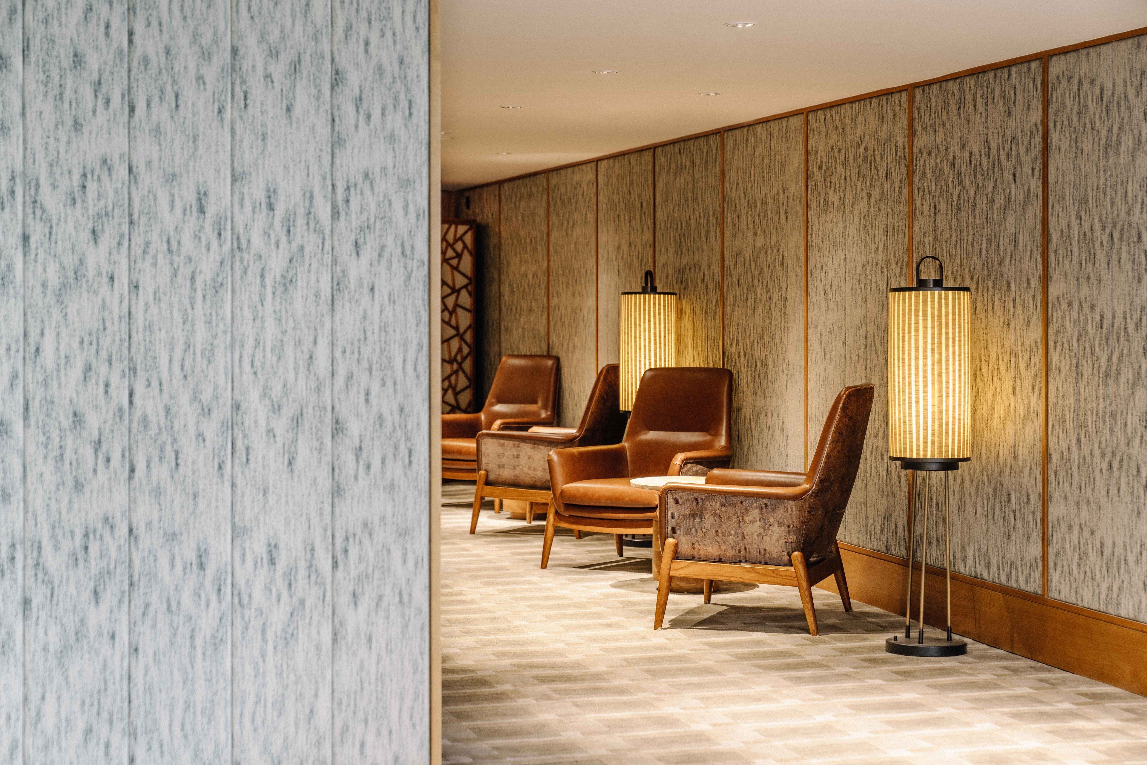 A hotel lobby with a patterned wall, three leather armchairs, and two floor lamps.