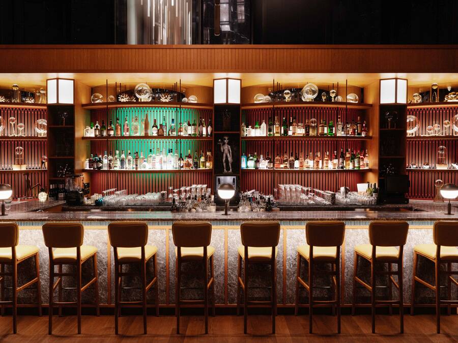 A bar area with multiple shelves of bottles and glasses, bar stools, and a central bar counter.