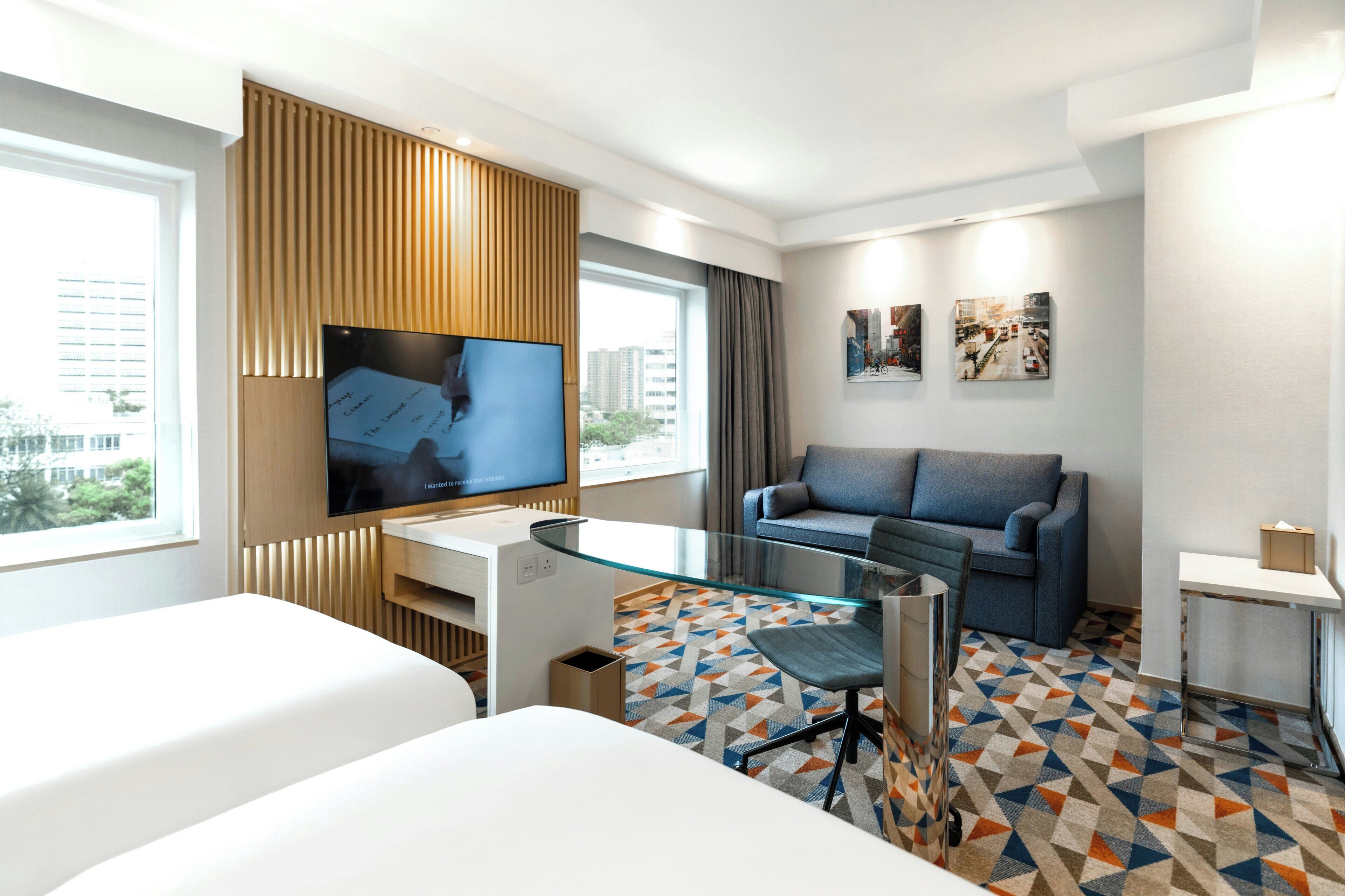 Una habitación de hotel con una cama, un escritorio, un televisor, un sofá y una alfombra estampada.