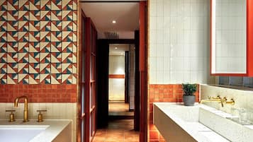 A modern bathroom with a geometric tile backsplash, dual sinks with gold fixtures, and a potted plant on the vanity.