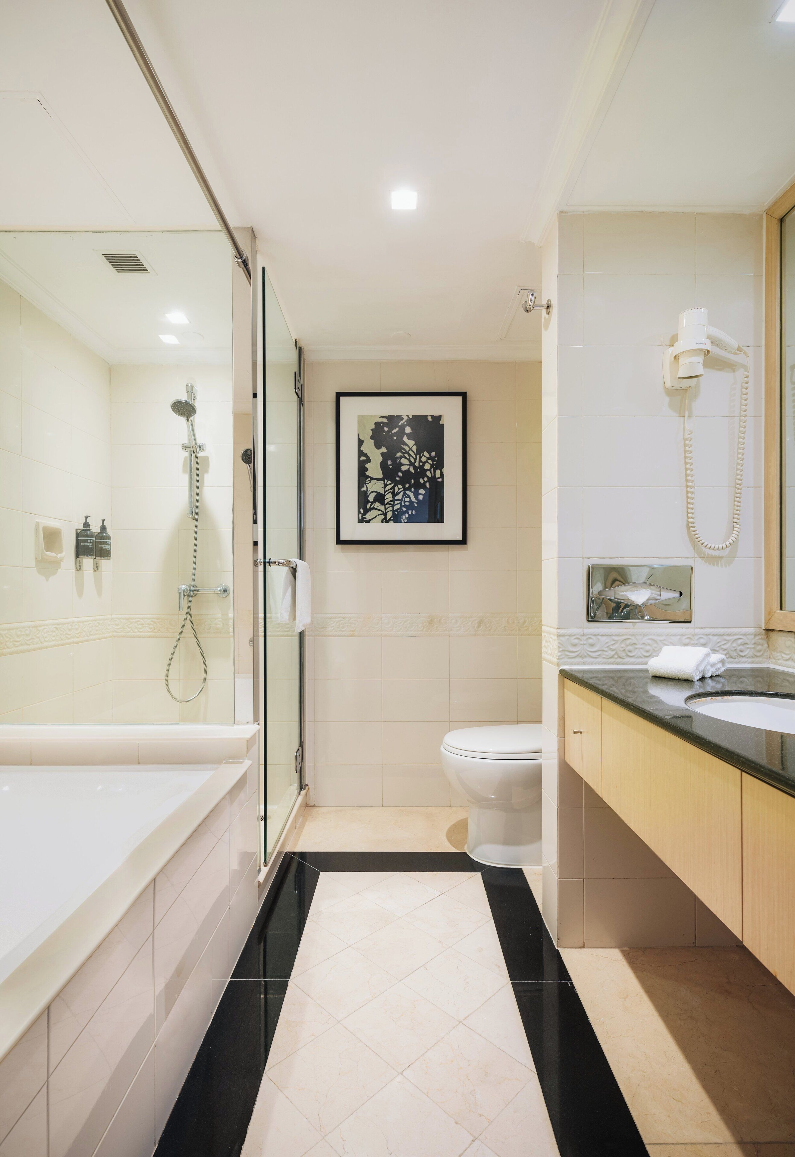 A modern bathroom with a glass-enclosed shower, a white toilet, and a vanity with a mirror and telephone.