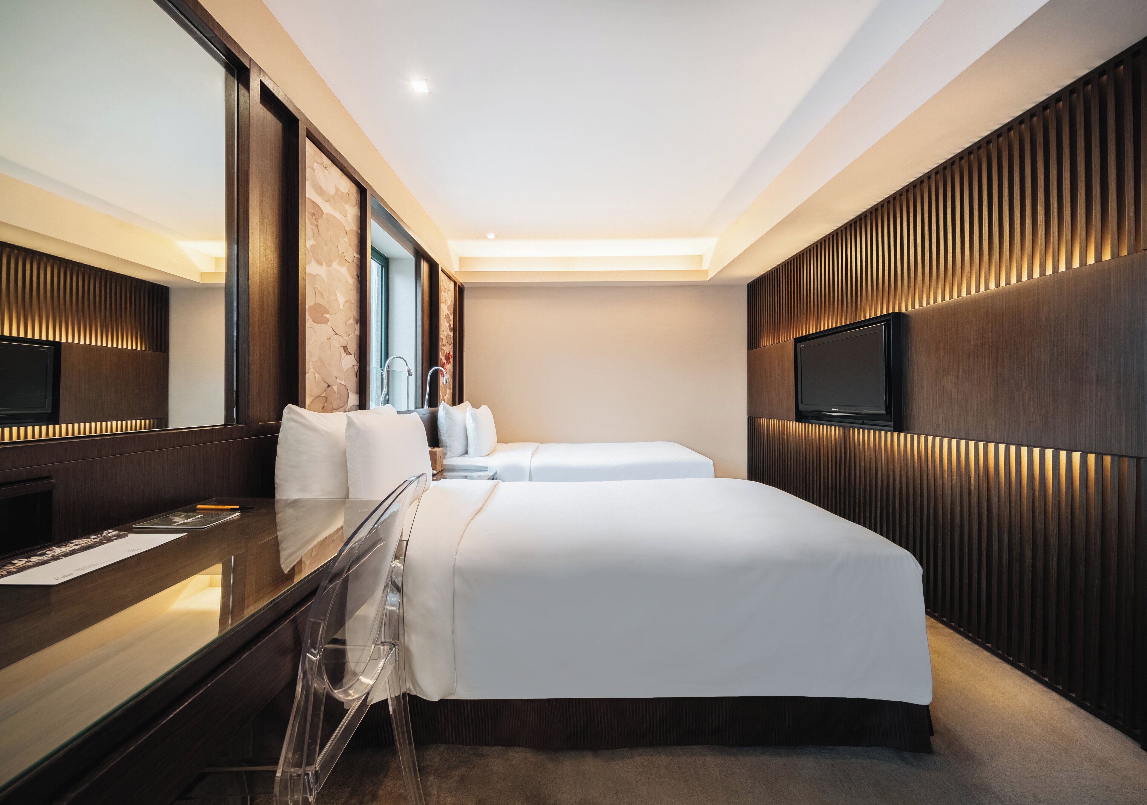 A modern hotel room with a large bed, a desk with a chair, a flat-screen TV, and a large mirror.