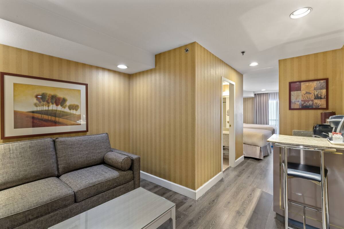 Une chambre d’hôtel équipée d’un canapé, d’une petite table, d’une kitchenette et d’une porte donnant sur une autre pièce.