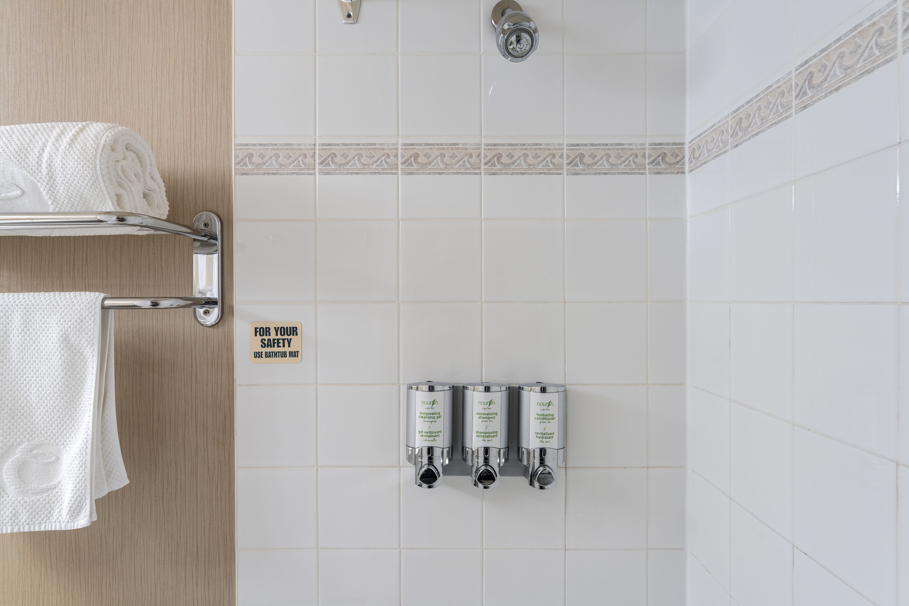 Un baño con toallero, ducha y tres dispensadores de champú fijos en la pared.