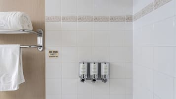 A bathroom with a towel rack, a shower, and three wall-mounted shampoo dispensers.