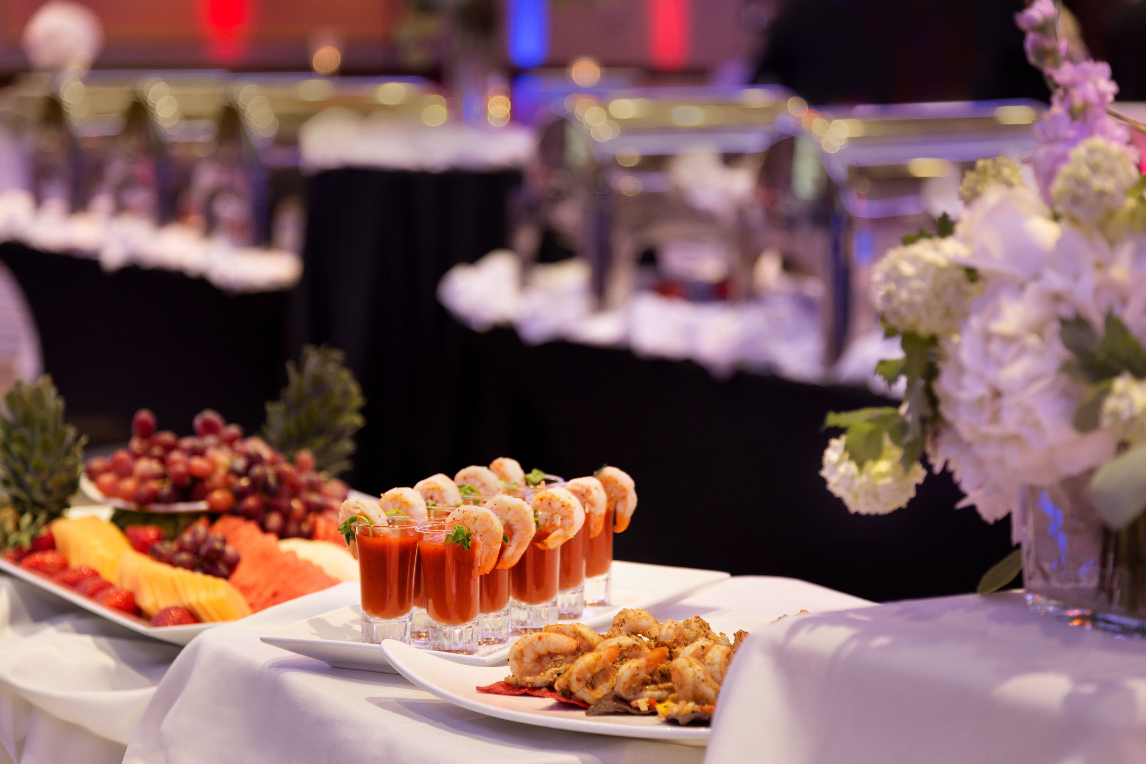 Una mesa de buffet con diferentes alimentos, incluyendo frutas, camarones y un vaso de jugo de tomate.