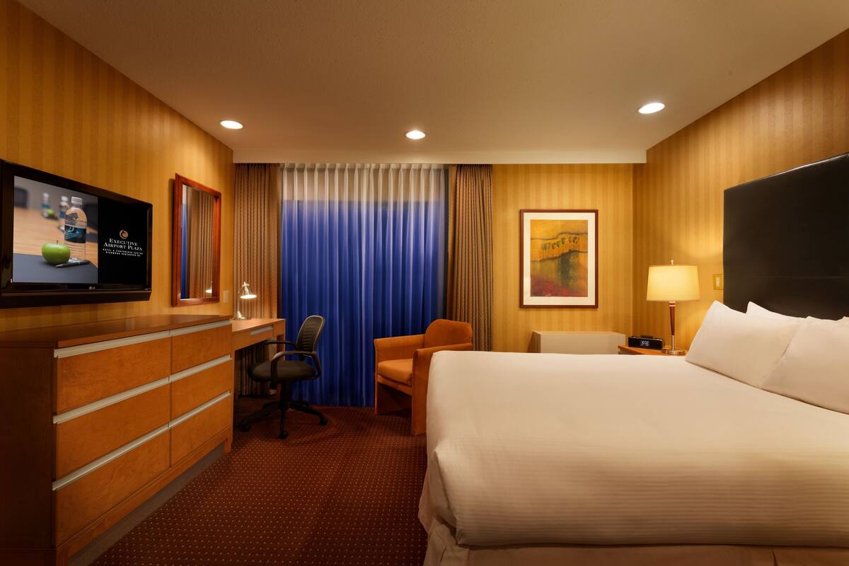 Une chambre d’hôtel équipée d’un lit, d’un bureau, d’une chaise, d’une télévision et d’œuvres d’art accrochées au mur.