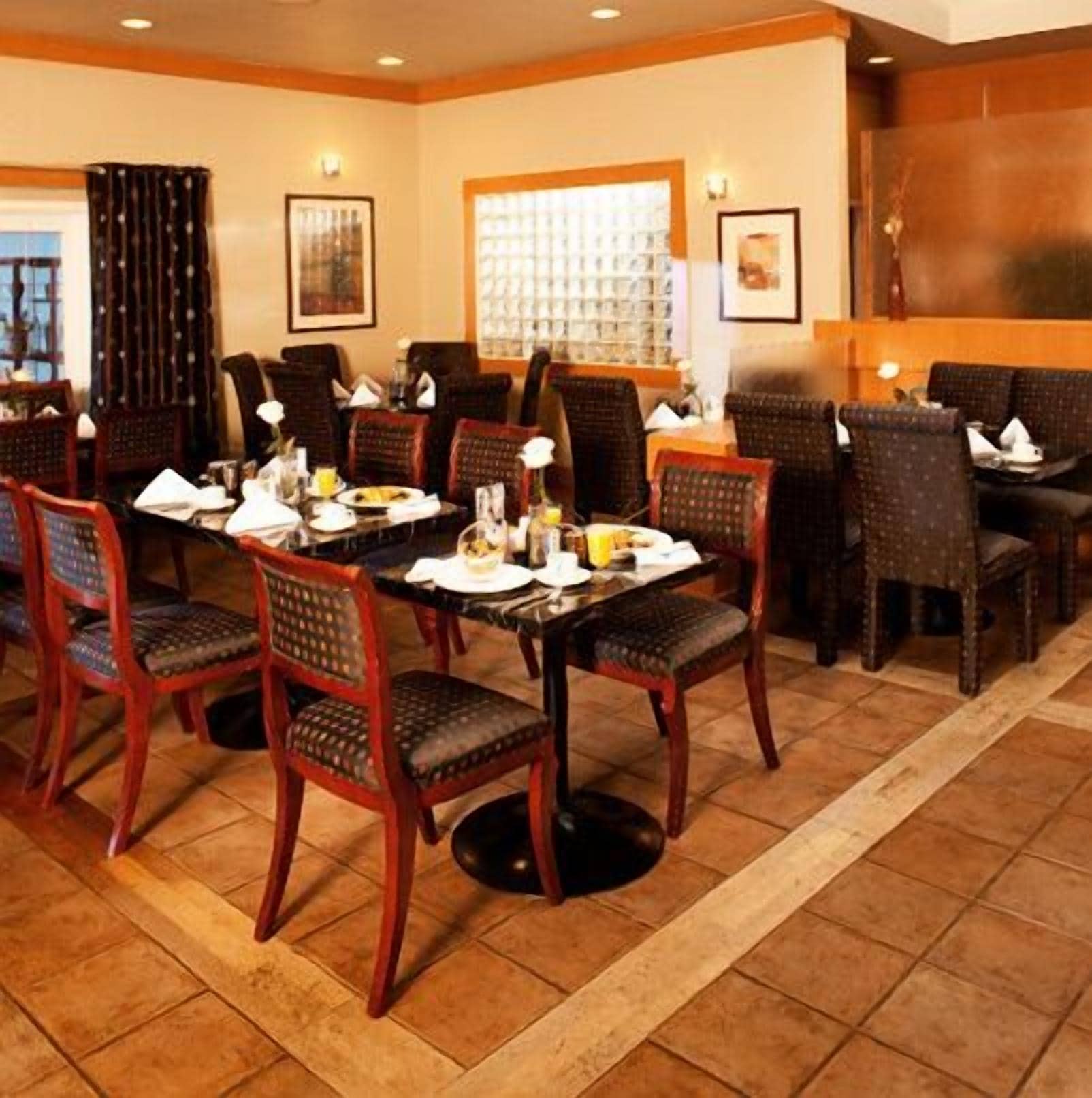 Un espace repas avec des chaises et des tables en bois, dont certaines sont dressées avec de la nourriture et des boissons.