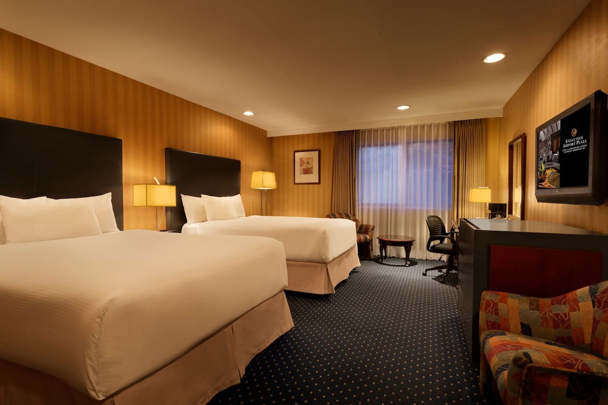 A hotel room with two beds, a desk, a chair, a television, and a window with curtains.