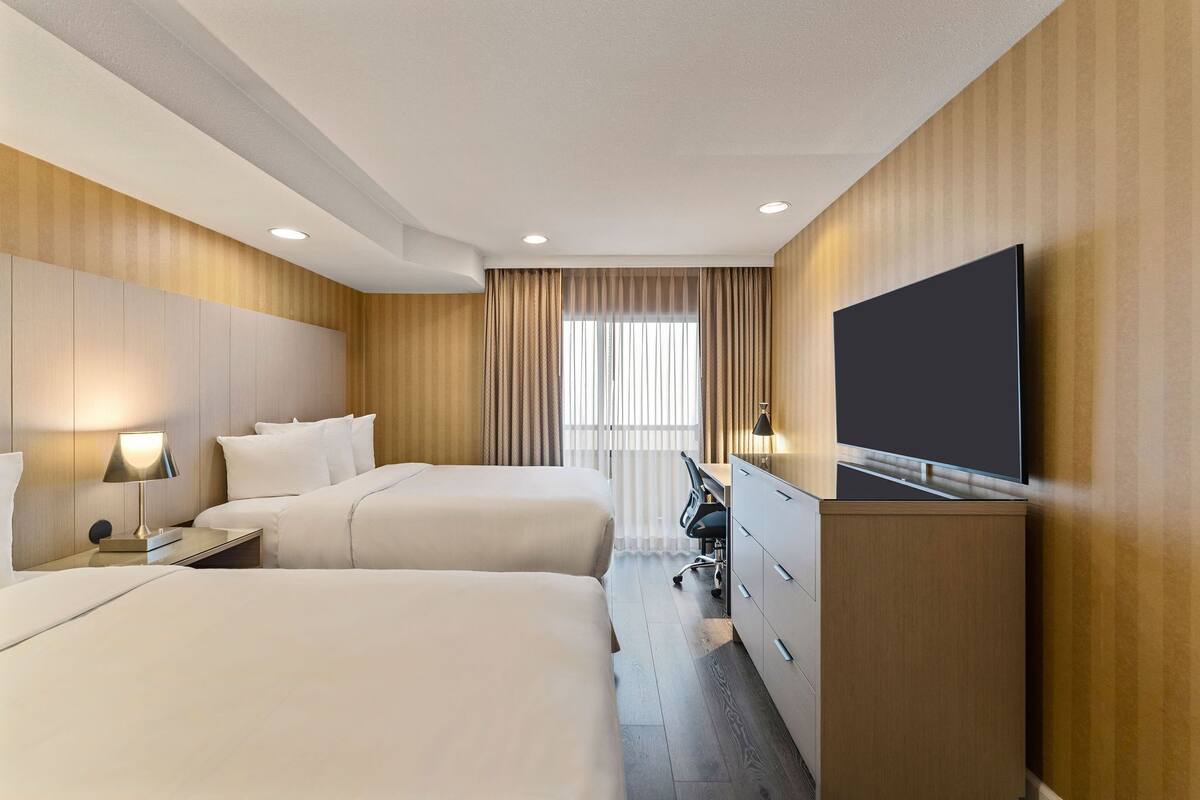 Une chambre d’hôtel avec deux lits, un bureau, une télévision et une fenêtre avec des rideaux.