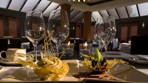 A dining table with three empty wine glasses and a dessert plate with a creamy dessert and decorative gold elements. - Executive Hotel Vancouver Airport (Richmond)