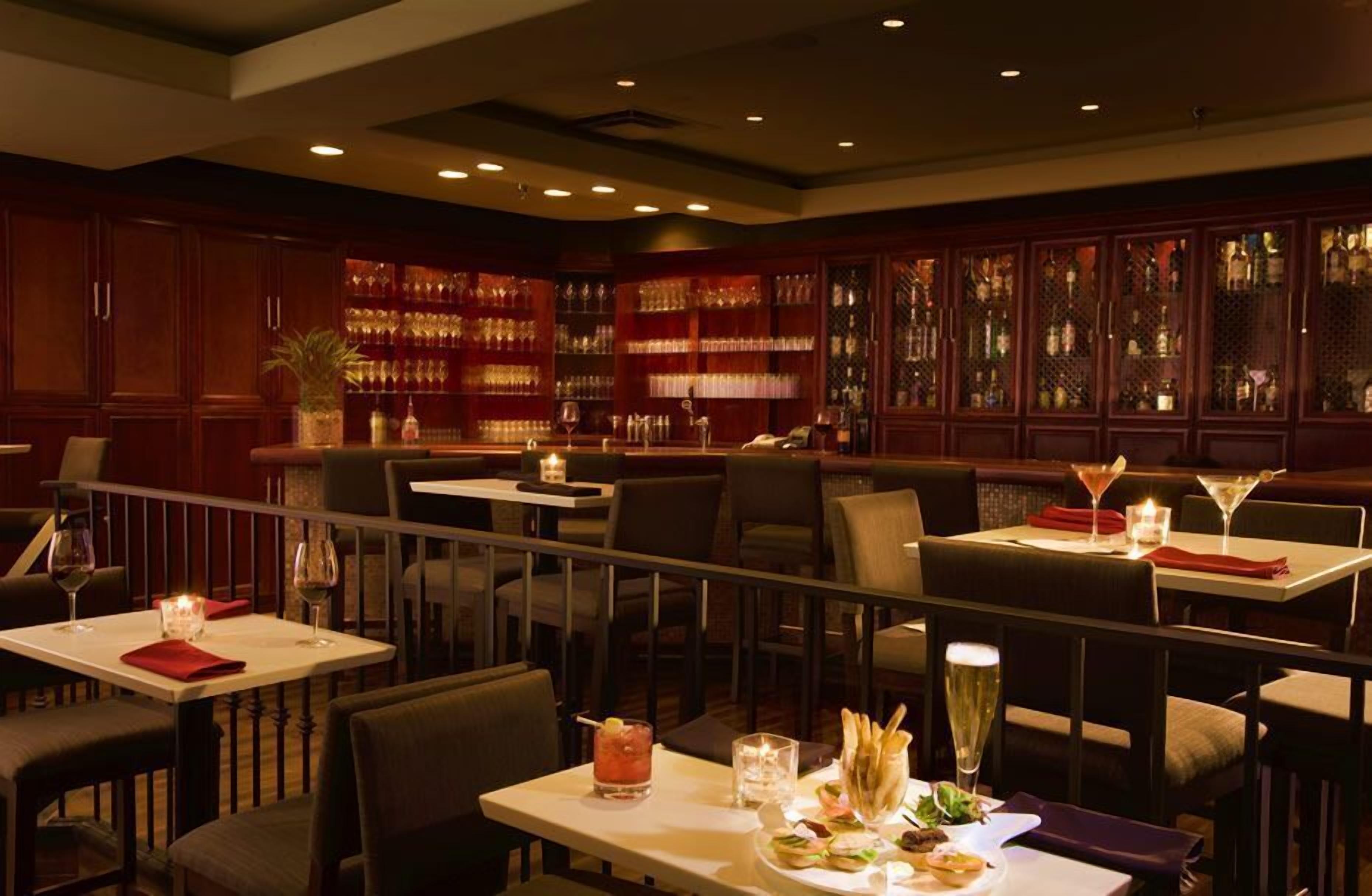 A restaurant with multiple tables, each set with wine glasses, a candle, and a menu.