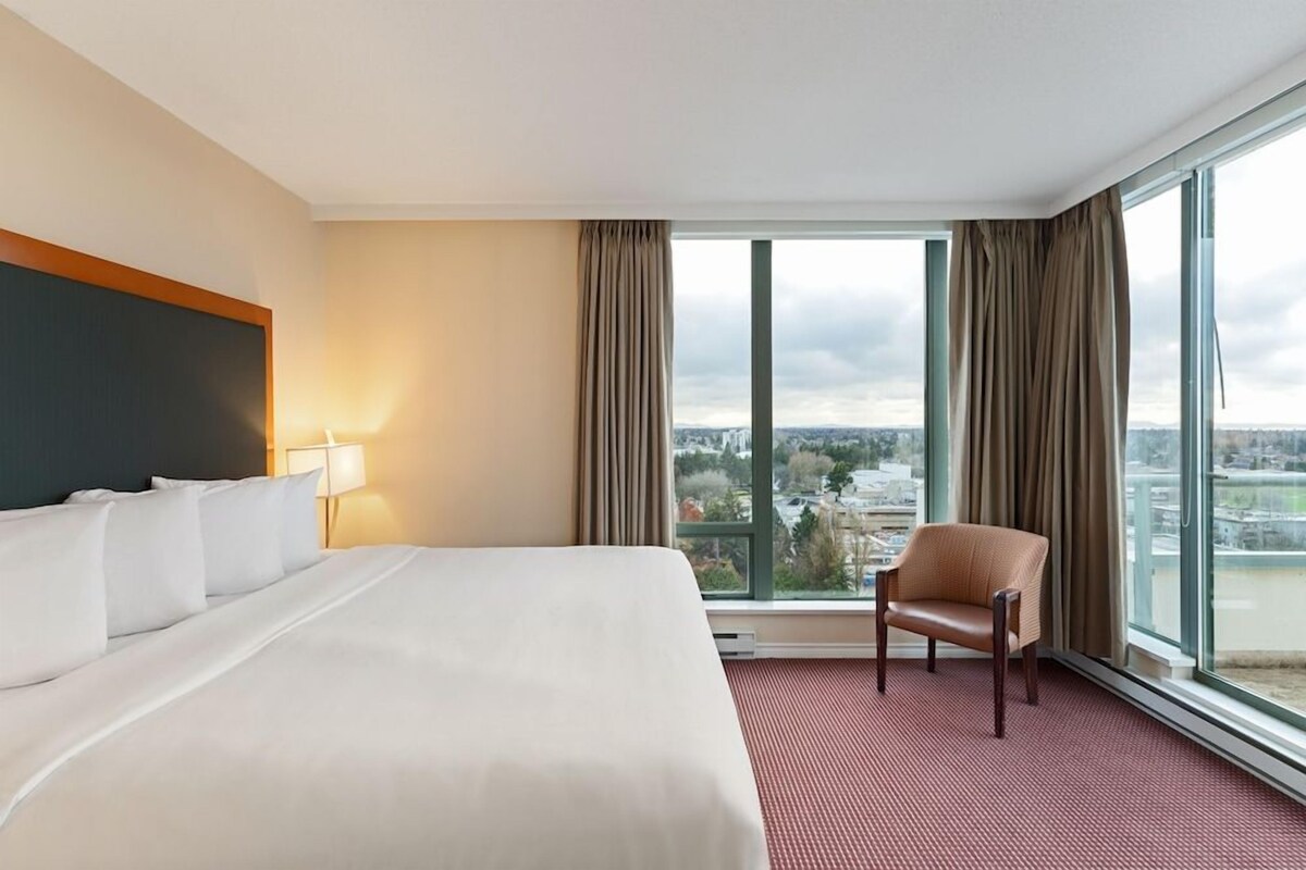 Une chambre d’hôtel avec un grand lit, une chaise et une vue sur le paysage urbain, grâce à de grandes fenêtres.
