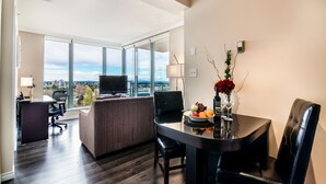 A modern hotel room with a large window, a dining area with a table and chairs, a sofa, a TV, and a city view. - Executive Hotel Vancouver Airport (Richmond)