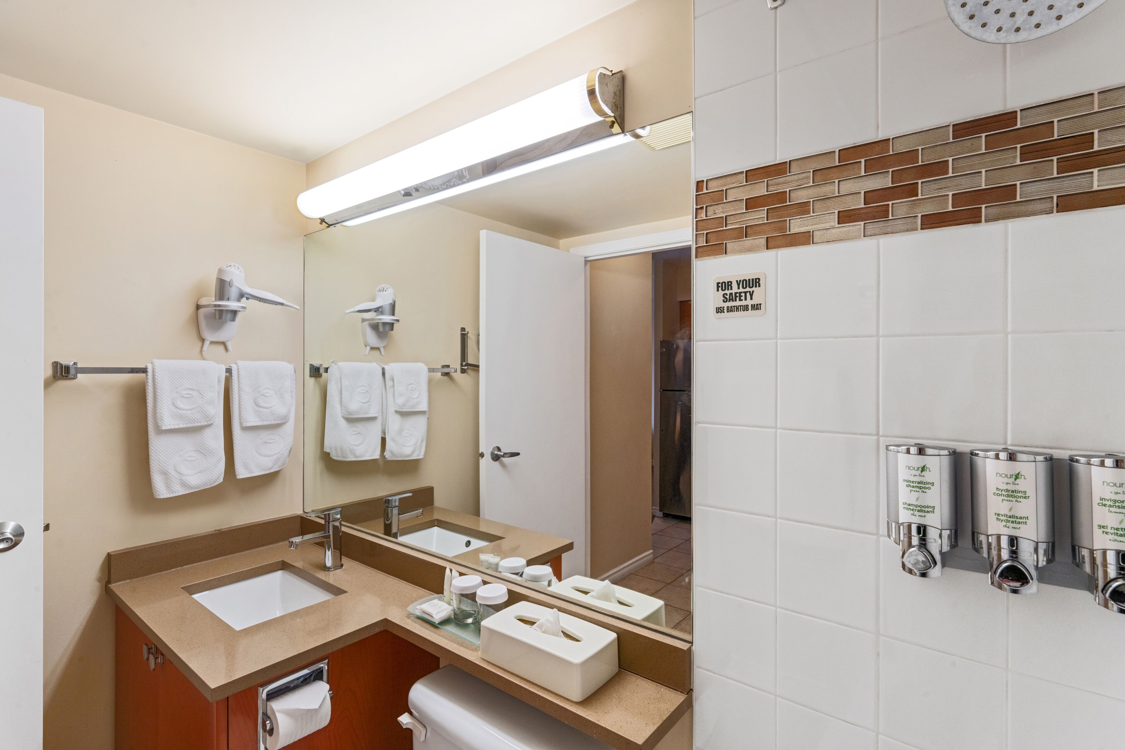 A modern bathroom with a large mirror, two sinks, a towel rack, and a shower area.