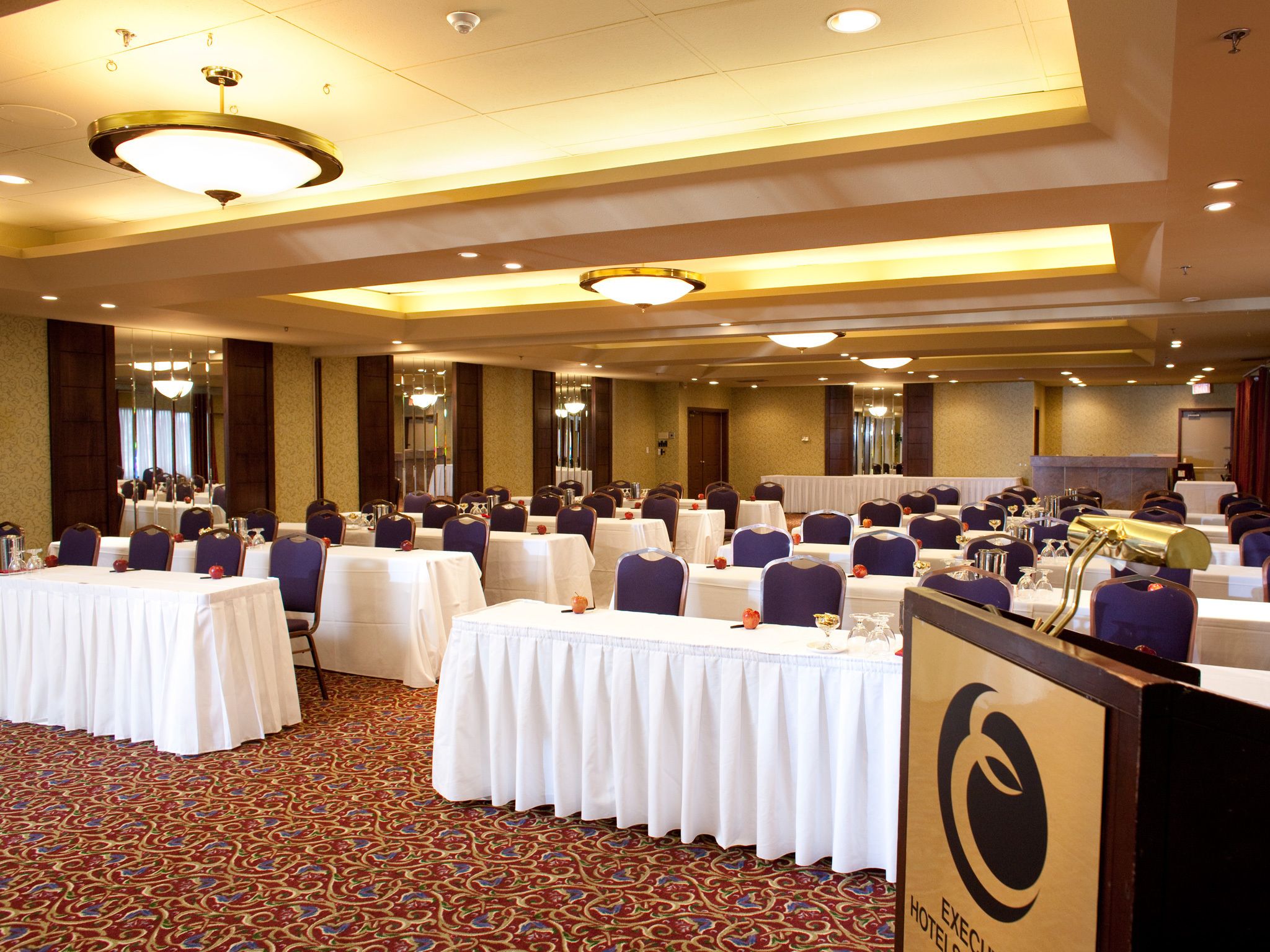 Un salón de conferencias con varias mesas, sillas y un atril con un logotipo.