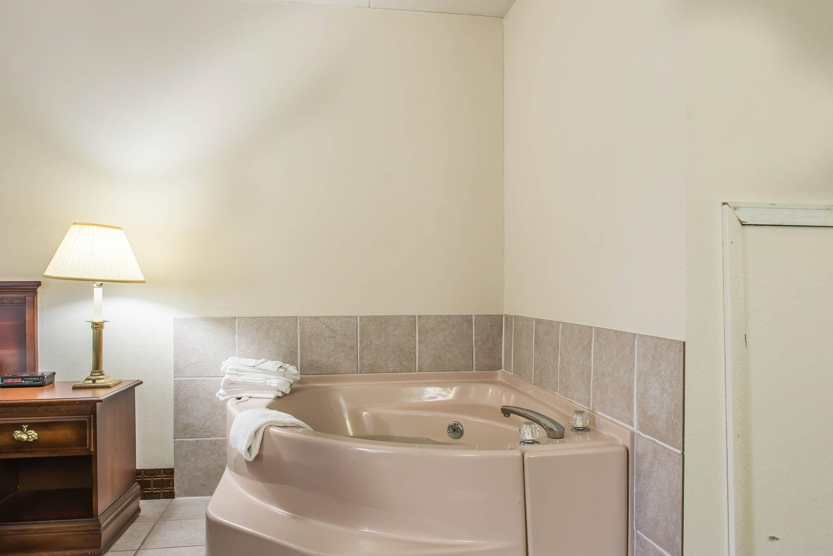 A bathroom with a bathtub, a vanity with a lamp, and a door.