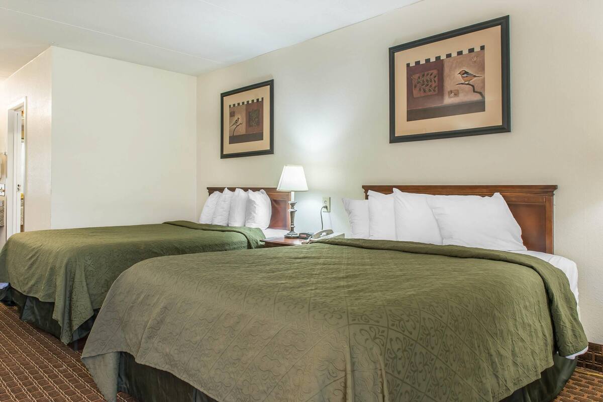 A hotel room with two beds, each with green bedding, a nightstand with a lamp, and two framed pictures on the wall.