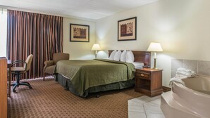 Habitación de hotel con cama, dos lámparas de noche, un escritorio con silla, una ventana grande con cortinas y una bañera.