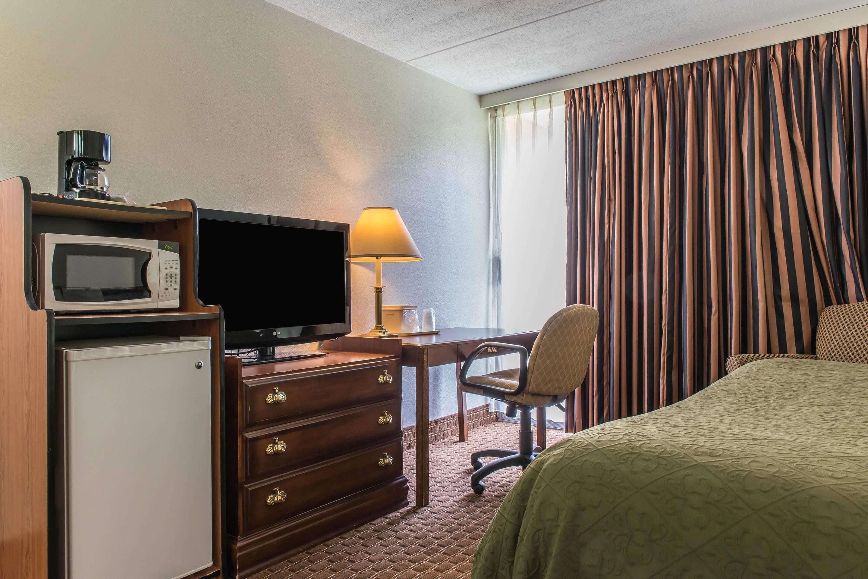 Une chambre d’hôtel équipée d’un lit, d’un bureau avec une lampe, d’une télévision, d’un four à micro-ondes et d’un réfrigérateur.