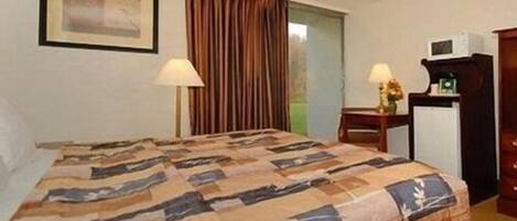 Ein Hotelzimmer mit einem Bett, zwei Nachttischlampen, einem Schreibtisch mit einer Mikrowelle und einem gerahmten Bild an der Wand.