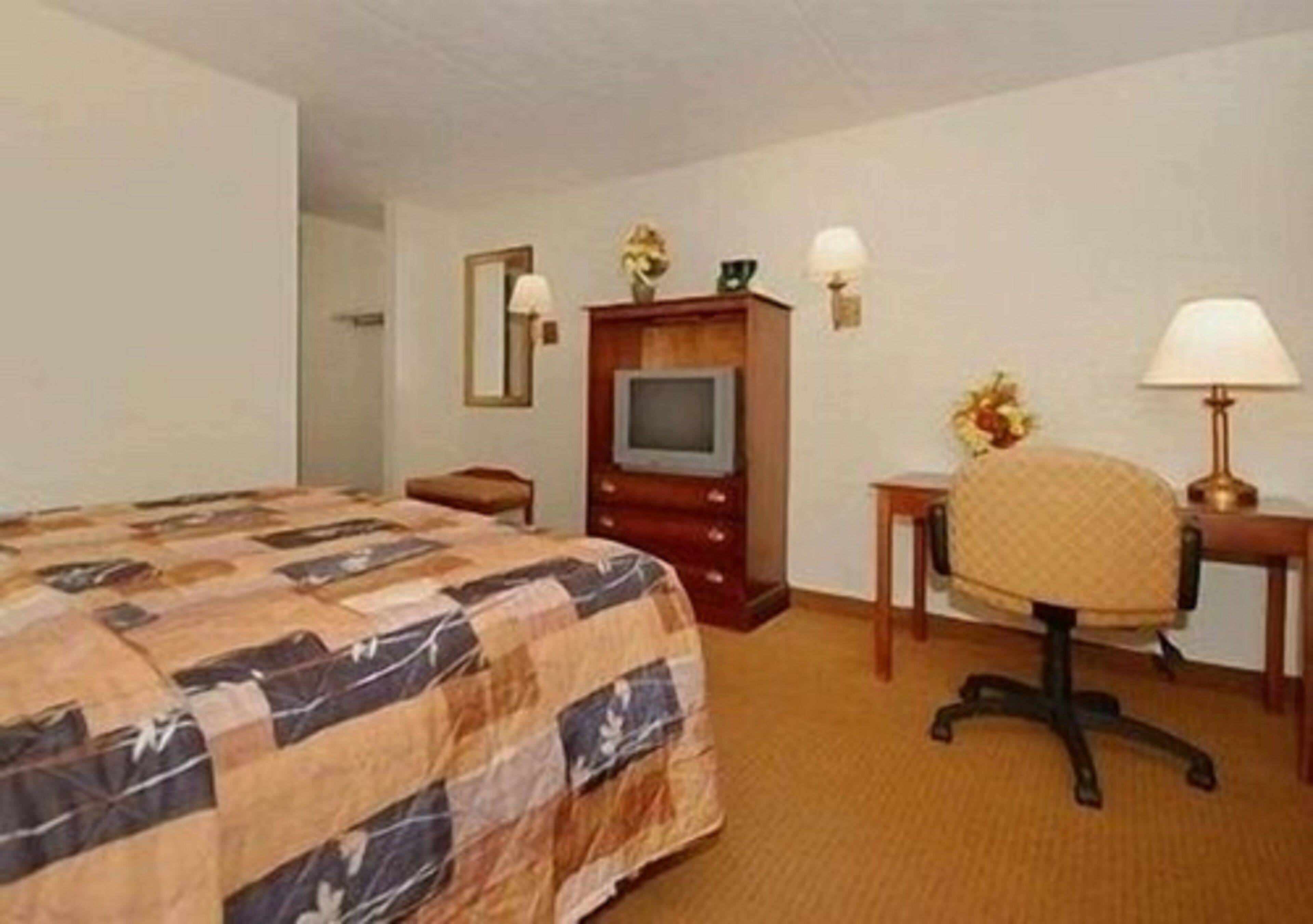 A hotel room with a bed, a desk, a chair, a television, and a lamp.