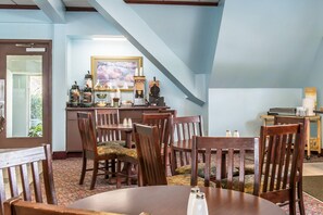 A dining area with wooden chairs and a table, a bar area with various bottles and a framed picture on the wall. - Rodeway Inn Brookville (Brookville)