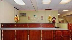 Un mostrador de recepción con acabado de madera, un logotipo en la parte superior y dos arreglos florales a cada lado.