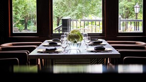 A dining table set for four with a vase of flowers, positioned by large windows with a view of a garden and a wooden deck. - Chateau Merrimack Resort & Spa (Tyngsboro)