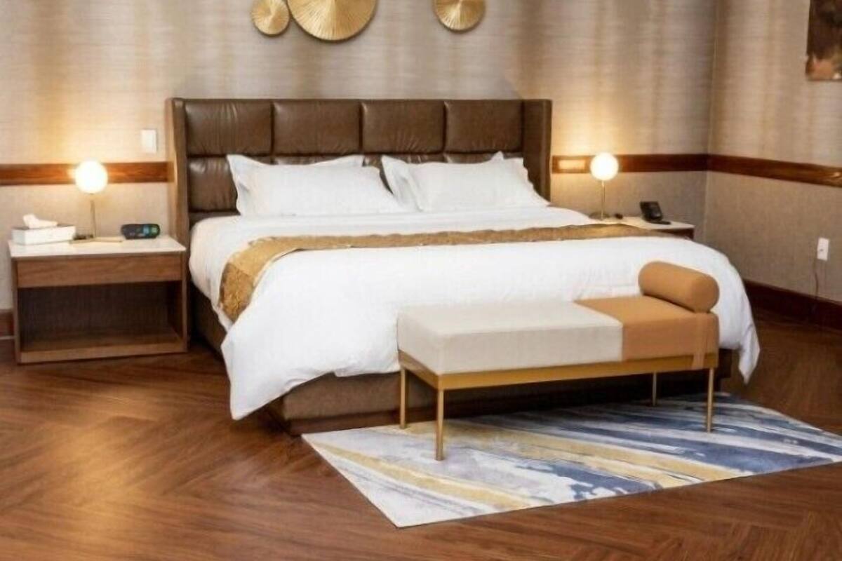 Ein Hotelzimmer mit einem großen Bett, Nachttischen, einer Bank und einem gemusterten Teppich.