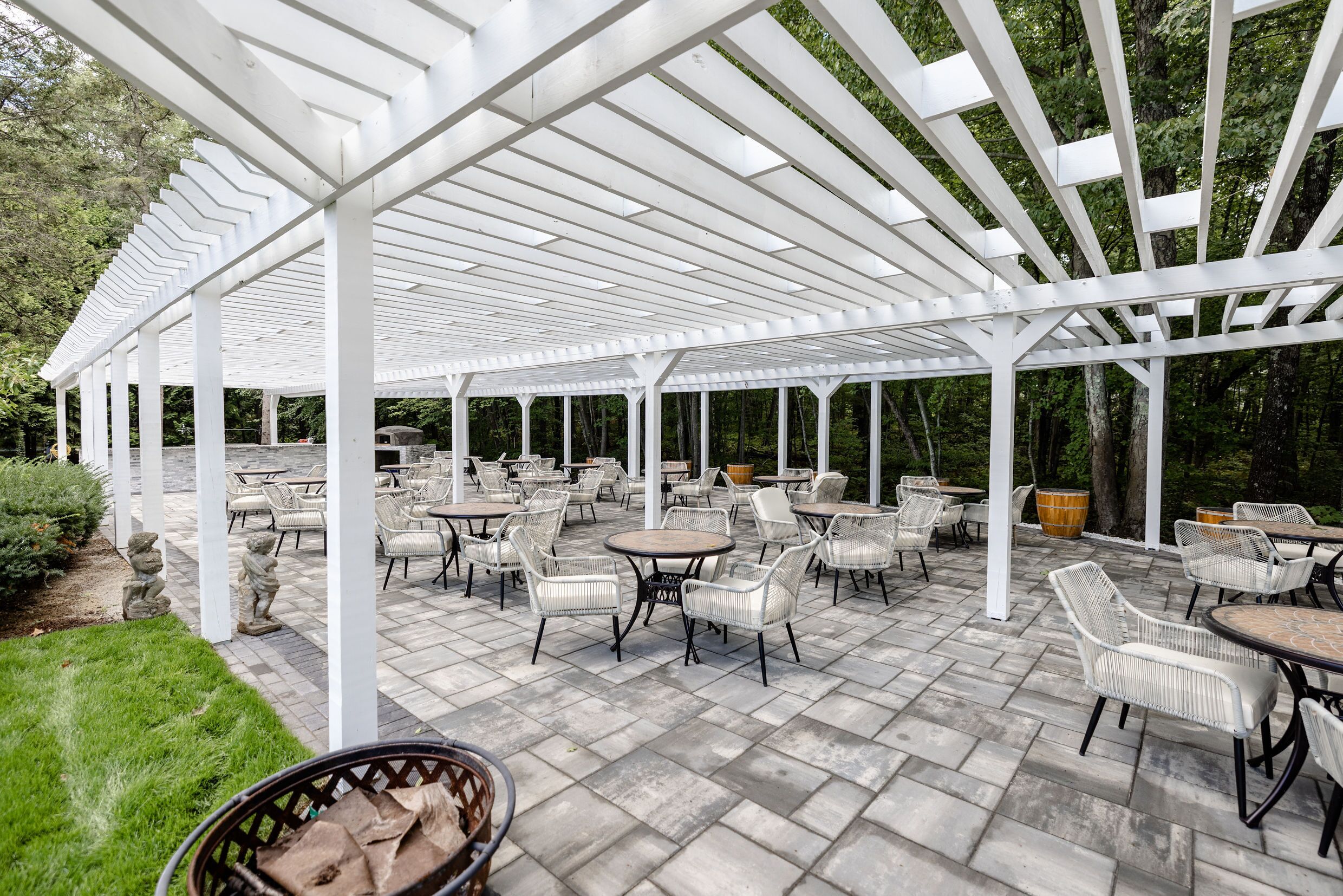 A covered patio area with white pergola structure, outdoor seating with wicker chairs and tables, and a stone pathway.