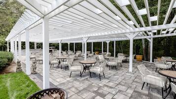 A covered patio area with white pergola structure, outdoor seating with wicker chairs and tables, and a stone pathway.
