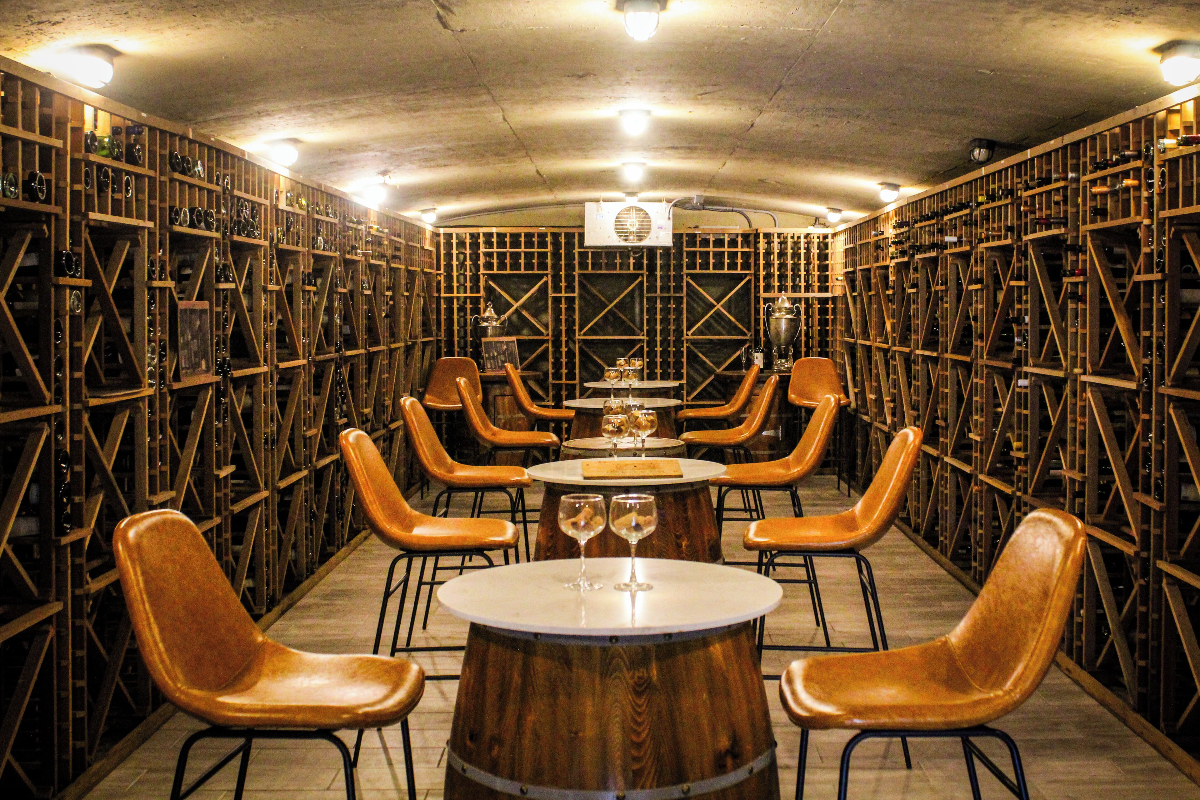 A wine cellar with wooden racks, a central table with chairs, and wine glasses.