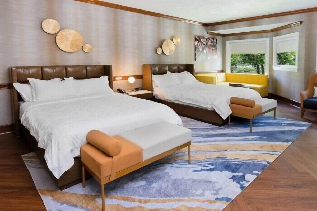 Ein Hotelzimmer mit zwei Betten, einem Sofa, einem Sessel und einem großen Fenster.