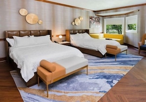 A hotel room with two beds, a sofa, a chair, and a large window.