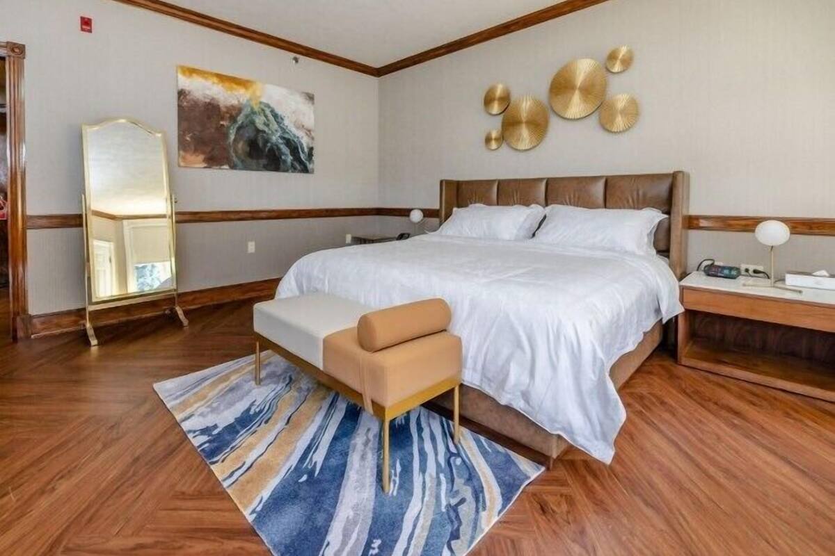 Ein Hotelzimmer mit einem großen Bett, einer Bank, einem Nachttisch, einem Spiegel und einem Bild an der Wand.