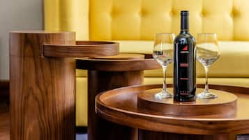A wooden table with a bottle of wine and two glasses on it, set against a yellow upholstered sofa.