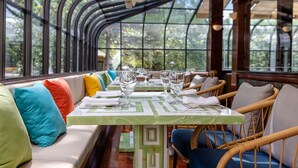 A restaurant with a long table set for dining, cushioned seating, and large windows offering a view of greenery. - Chateau Merrimack Resort & Spa (Tyngsboro)