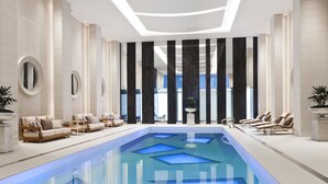 A modern indoor pool area with geometric light patterns, lounge chairs, and a view of the outside. - Rosewood Hotel Georgia (Vancouver)