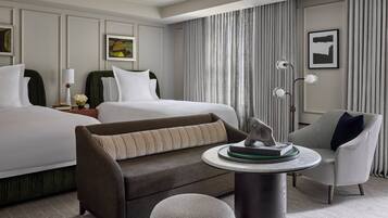A hotel room with two beds, a sofa, a small table with a book, and a lamp.